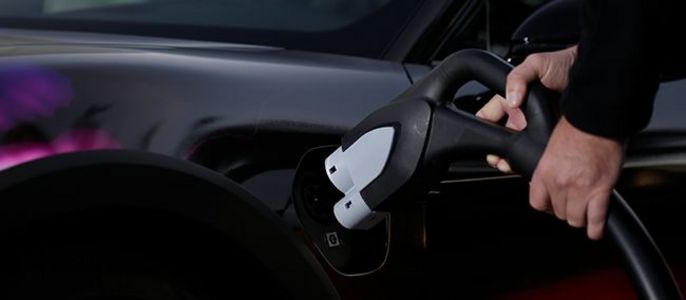 Eine Person hält eine schwarze Ladestation in der Hand und schließt sie an ein Auto mit einem eleganten Design an.