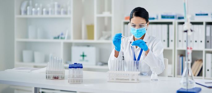 Eine Frau in einem Laborkittel und blauen Handschuhen arbeitet mit einem Reagenzglas.