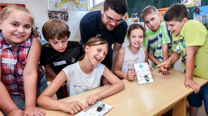 Eine Gruppe von Kindern und ein Erwachsener in einem Klassenzimmer, die TUEV Kids Strom Bausätze zusammenbauen.