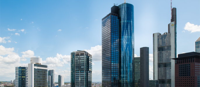 Eine Stadtsilhouette mit hohen, modernen Wolkenkratzern, einige mit spiegelnden Glasfassaden, vor einem klaren, blauen Himmel mit ein paar vereinzelten Wolken.