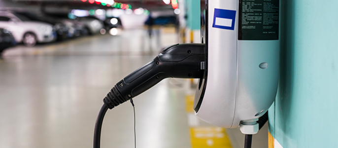 Eine Ladestation für Elektrofahrzeuge, die an einer Wand in einem Parkhaus montiert ist, mit mehreren geparkten Autos im Hintergrund.