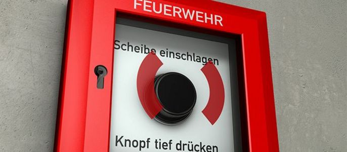 Ein roter Feuermelder mit der Aufschrift "FEUERWEHR", "Scheibe einschlagen" und "Knopf tief druecken".