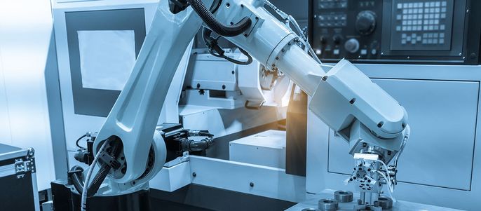 Ein Roboterarm in einer Fabrikumgebung, der mit einer Maschine interagiert.